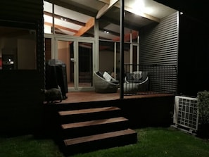 Ein modernes Haus mit überdachter Terrasse, einer Treppe zu einer Tür und einem kleinen Garten.