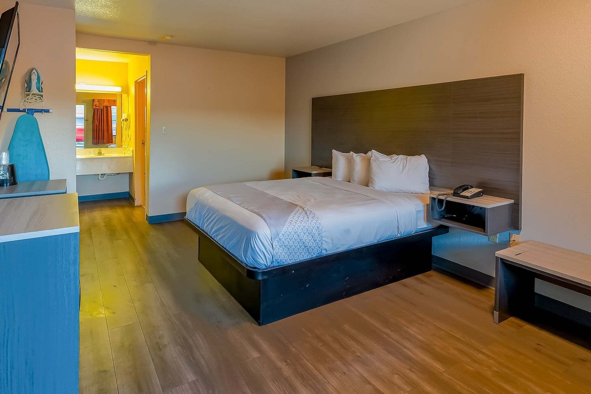 A modern hotel room with a large bed, bedside tables, a desk, and a mirror.