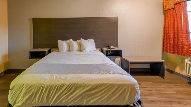 Habitación de hotel con una cama grande, mesitas de noche, cabecera y una ventana con cortinas.