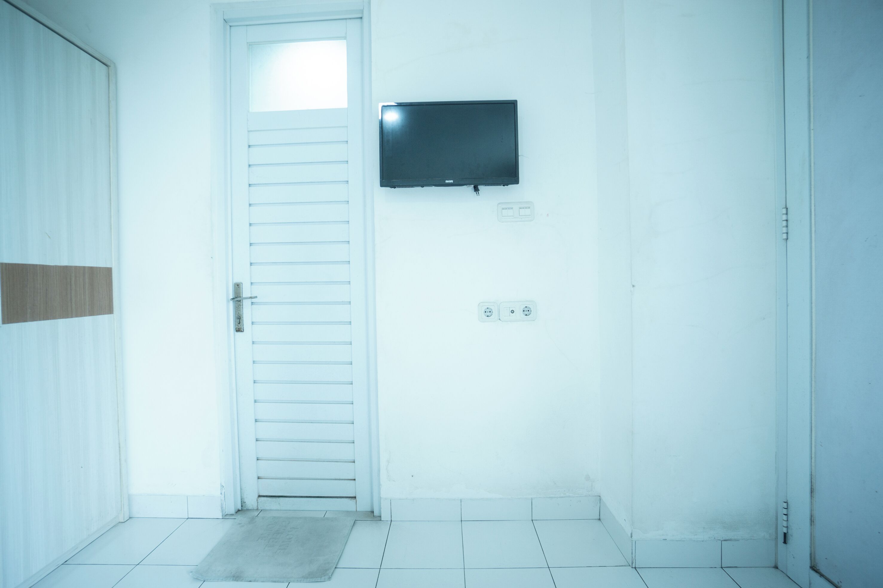A room with a white door, a flat-screen TV mounted on the wall, and a tiled floor.