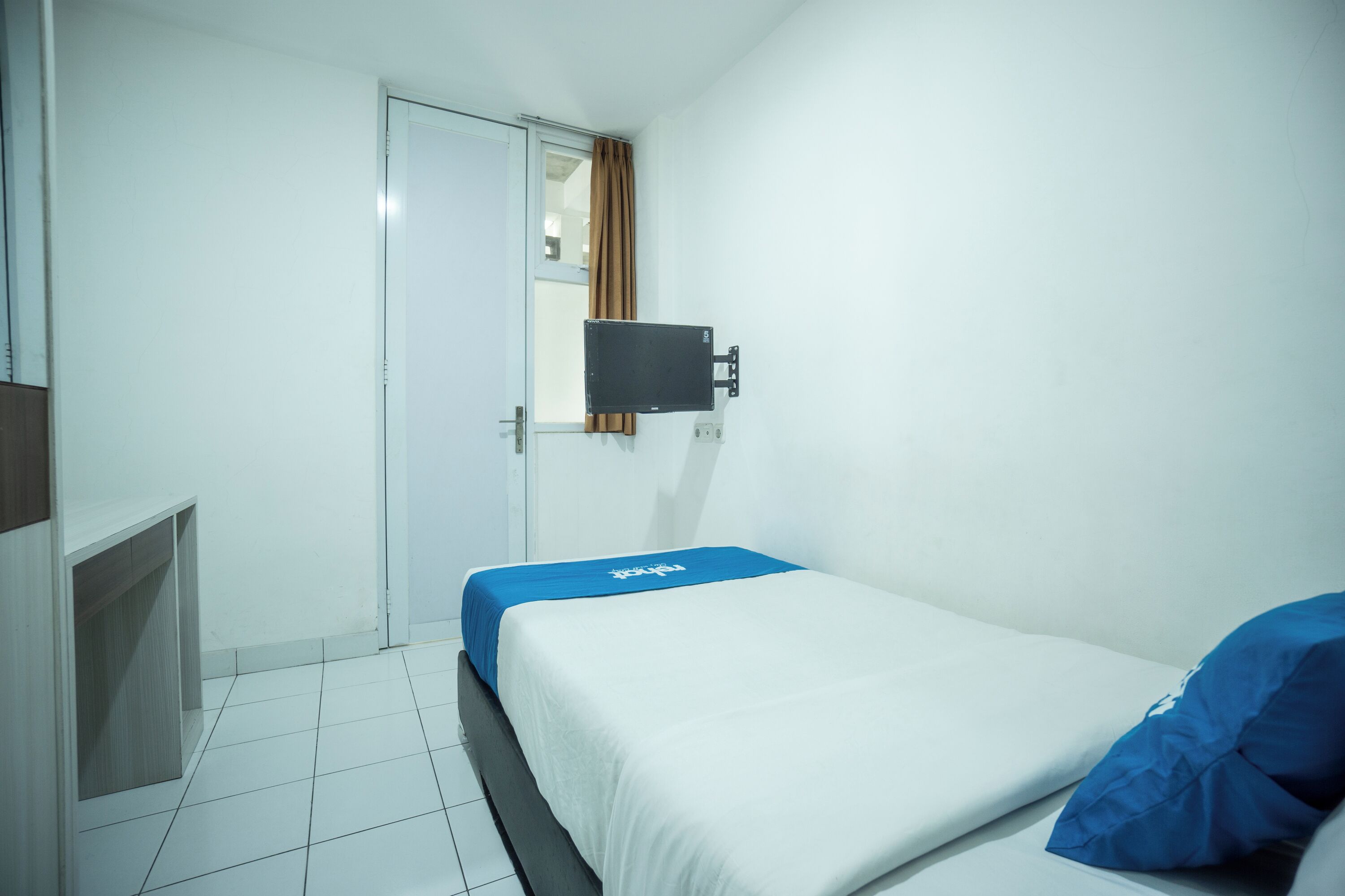 A room with a bed, a TV mounted on the wall, and a door.
