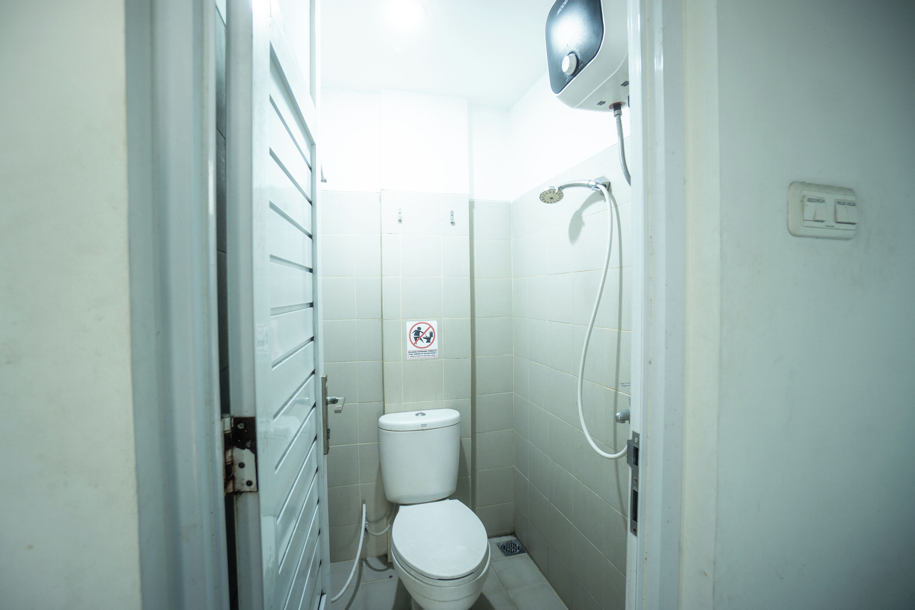 Une petite salle de bain étroite, équipée de toilettes, d’une douche et d’un sèche-mains.