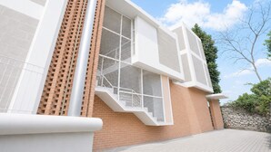 A modern building with a brick facade, large windows with white frames, and a clear sky. - Rehat at Alamanda 7 Syariah Guest House (Bandung)