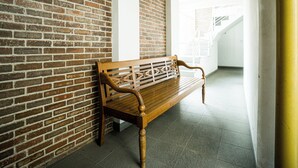 A wooden bench against a brick wall in a hallway with a tiled floor and a white door. - Rehat at Alamanda 7 Syariah Guest House (Bandung)