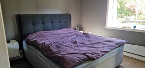 A bed with a headboard, a bedside table, and a window with a view of trees. - Charming house, 8 beds, possibility to rent a boat (Bjørnafjorden)