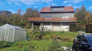 Une maison à deux étages avec un balcon, une serre et une voiture garée dans l’allée.