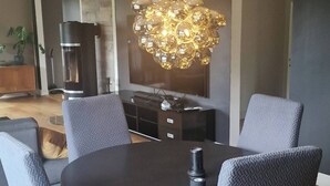 Un coin repas comprenant une table ronde, six chaises grises à revêtement rembourré, un lustre moderne et une machine à café.