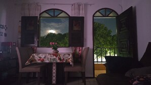 Ein Essbereich mit Tisch für zwei Personen, einer Blumenvase und Blick durch ein Fenster mit Rollläden.