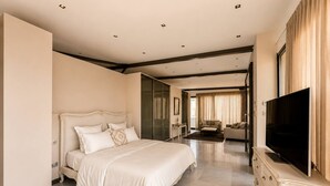 A spacious hotel room with a large bed, a TV, and a seating area with a sofa and armchair. - Villa Solis - Elegant Villa with Private Pool (Marsa)
