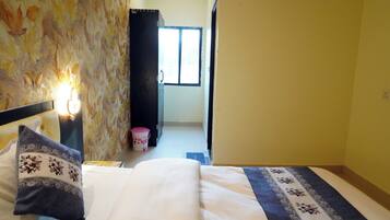 Habitación de hotel con cama, mesita de noche con lámpara, ventana y puerta que da a otra habitación.
