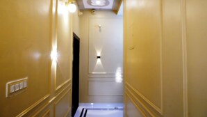 Un couloir étroit, avec une porte blanche au fond, des spots encastrés et un interrupteur sur le mur.
