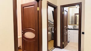 Une porte en bois avec une poignée en laiton, un miroir sur le mur adjacent, et, au fond, on aperçoit un lit et une salle de bain.