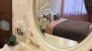 Een slaapkamer met een grote spiegel, een bed met beddengoed met dessin en een decoratief hoofdeinde.