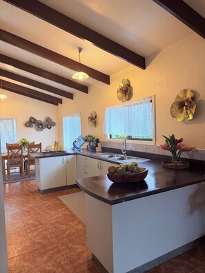 A modern kitchen with a central island, white cabinetry, and decorative wall art. - Mountain Views, 3BR Family Home, Near Muri Beach (Takitumu District)