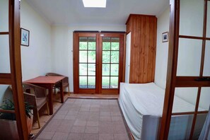 A room with a bed, a table, chairs, a potted plant, and a sliding glass door leading to a garden.