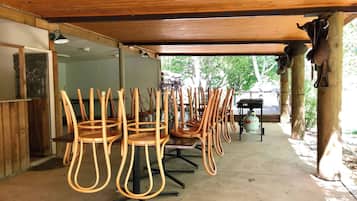 An outdoor covered dining area with wooden chairs and a table, a barbecue grill, and a gas cylinder.