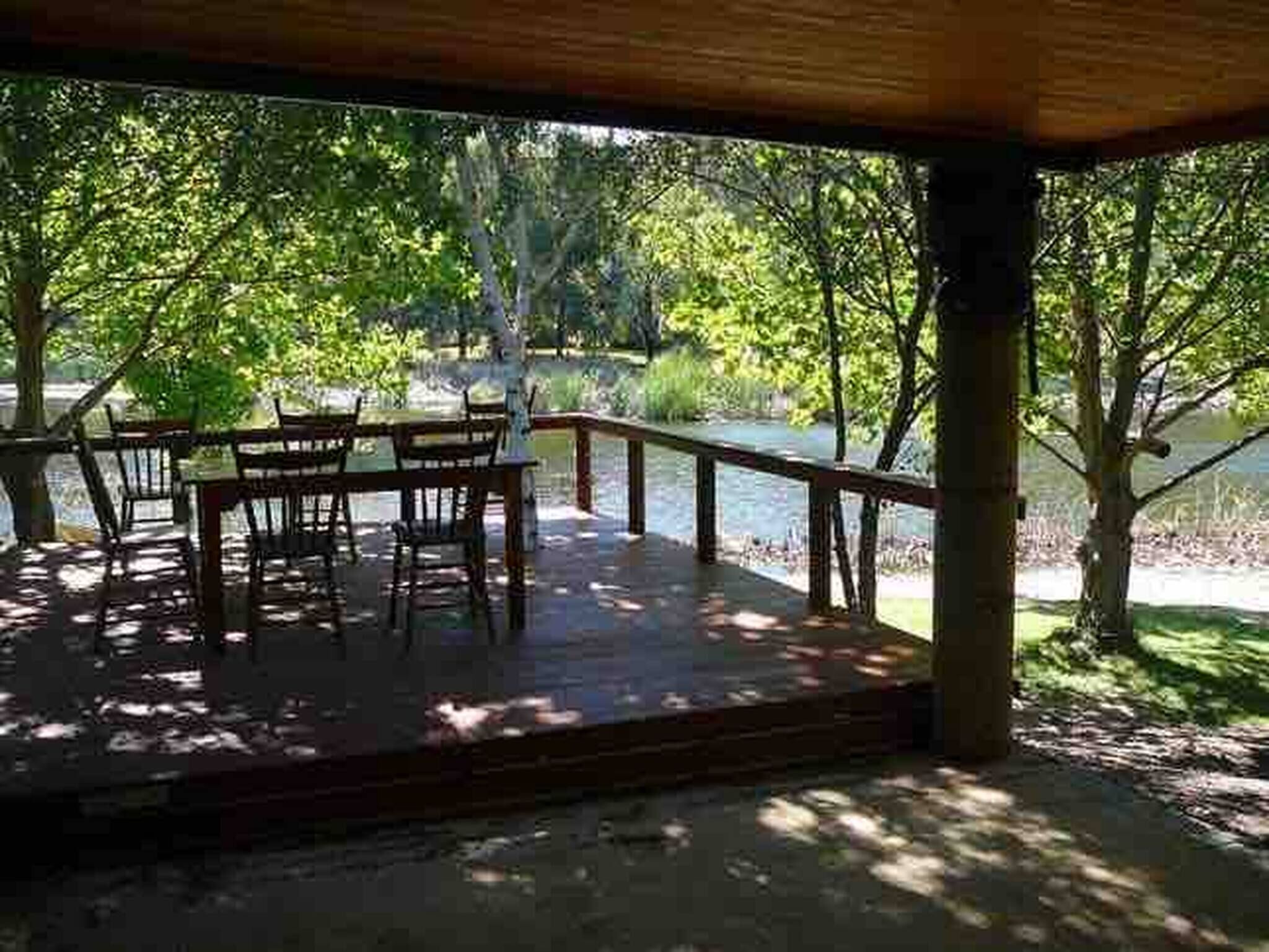 Terraza al aire libre con mesa y sillas, rodeada de árboles y vista a un cuerpo de agua.