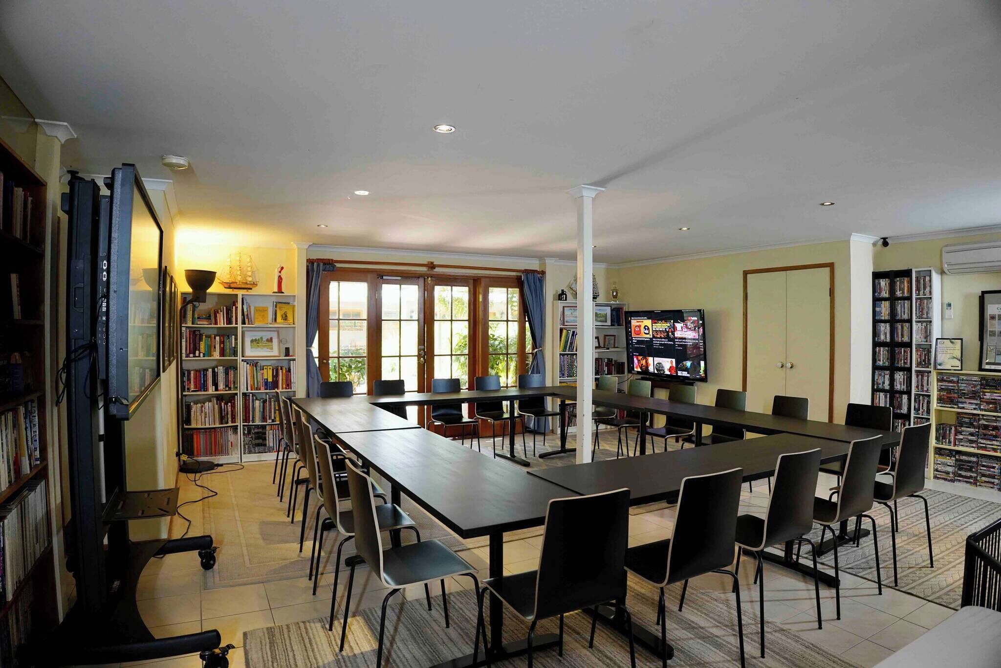 A spacious room with a long table, chairs, a television, and bookshelves.