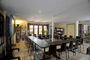 A spacious room with a long table, chairs, a television, and bookshelves.