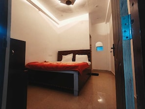 A bedroom with a bed, a TV, a skylight, and a door with a blue handle. - Maa Vindhyavasini Guest House (Gorakhpur)