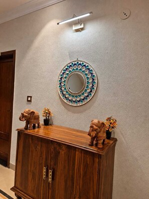 A room with a wooden cabinet, a decorative mirror, and two elephant figurines on top. - Vaanam One (Ujjain)