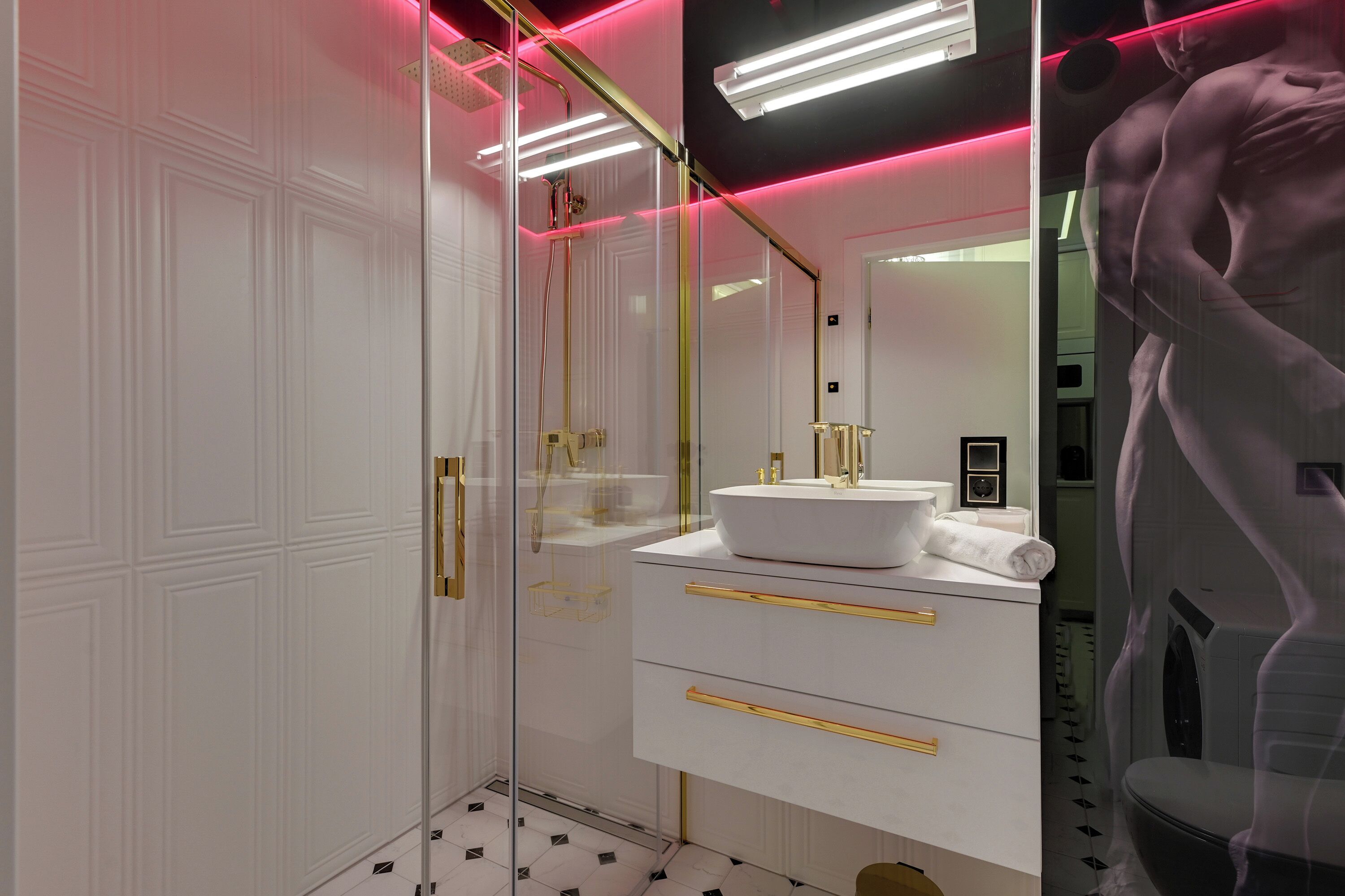 Une salle de bain moderne avec une douche à l’italienne en verre, un meuble-lavabo blanc avec des poignées dorées et un grand miroir.