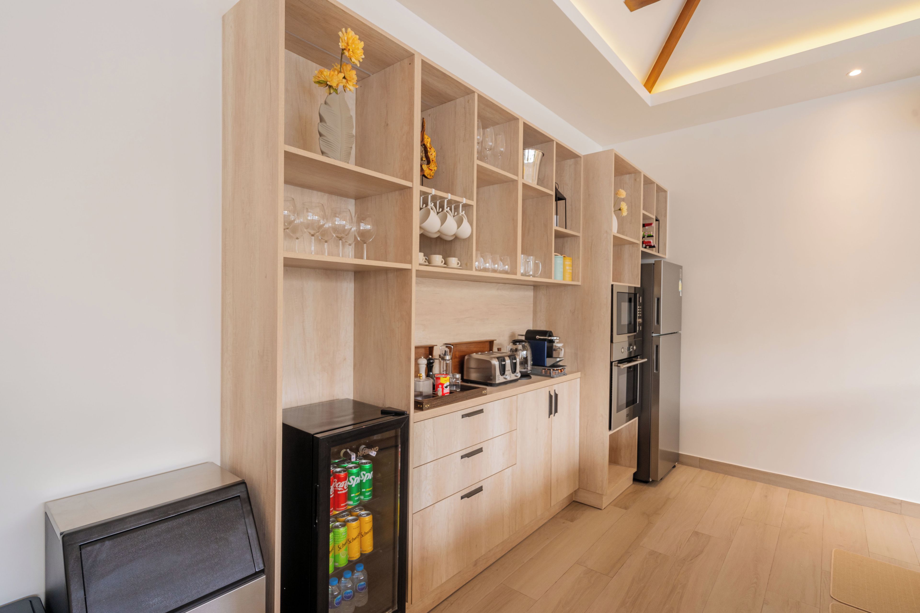A modern kitchen with wooden cabinets, a refrigerator, a coffee machine, and a beverage dispenser.