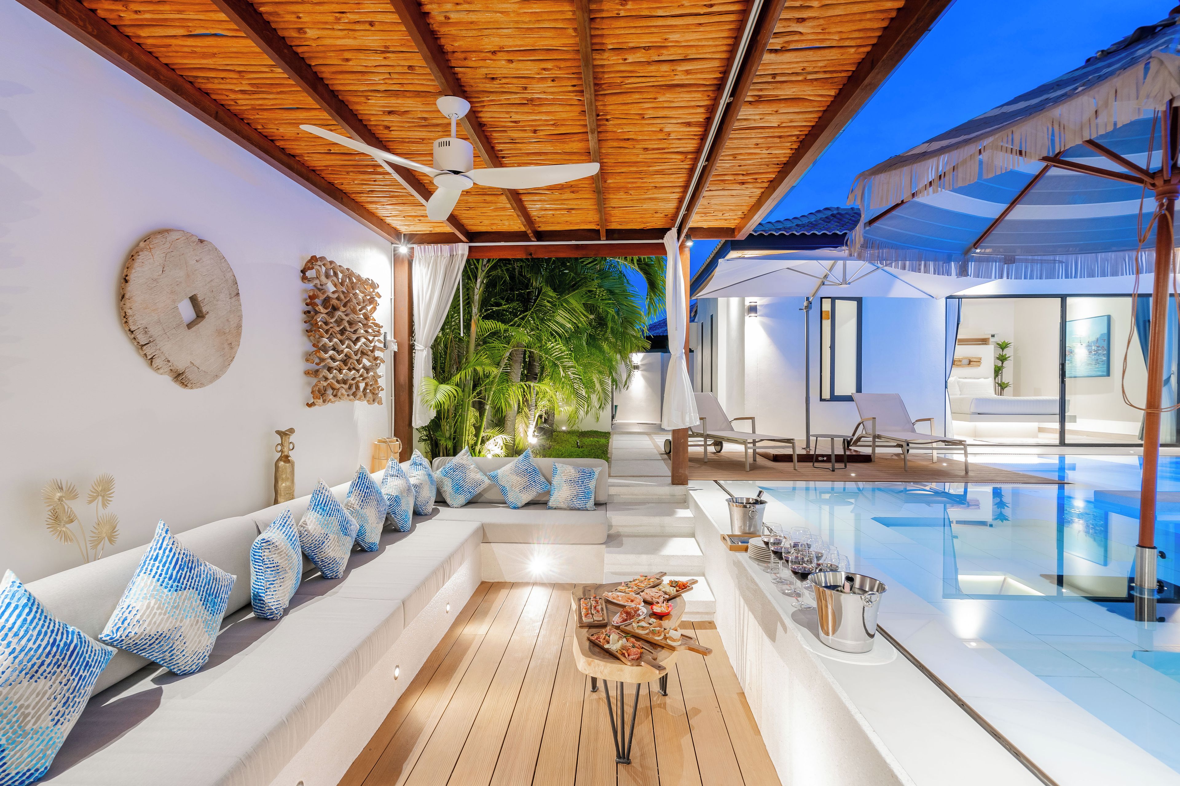 A modern outdoor pool area with a wooden deck, a seating area with patterned cushions, and a ceiling fan.