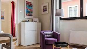 A room with a white cabinet, a purple armchair, a small table, and a window with a view of buildings. - Milan-Bergonzoli-Hugo - 1 apartment BDR (Milano)