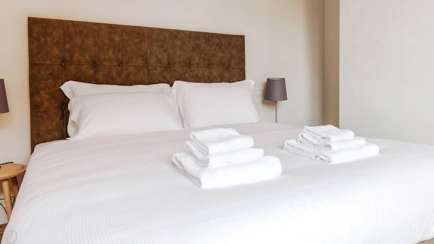 A neatly made bed with a brown headboard, white pillows, and a stack of folded white towels. - Milan-Bergonzoli-Hugo - 1 apartment BDR (Milano)