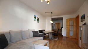 A modern living room with a sofa, coffee table, dining table, and chairs. There is a wooden cabinet and a door leading to another room. - Apartment in Strengen with mountain views (Strengen)