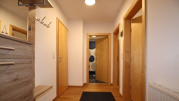 A hallway with wooden flooring, a black mat at the entrance, and wooden doors on both sides. - Apartment in Strengen with mountain views (Strengen)