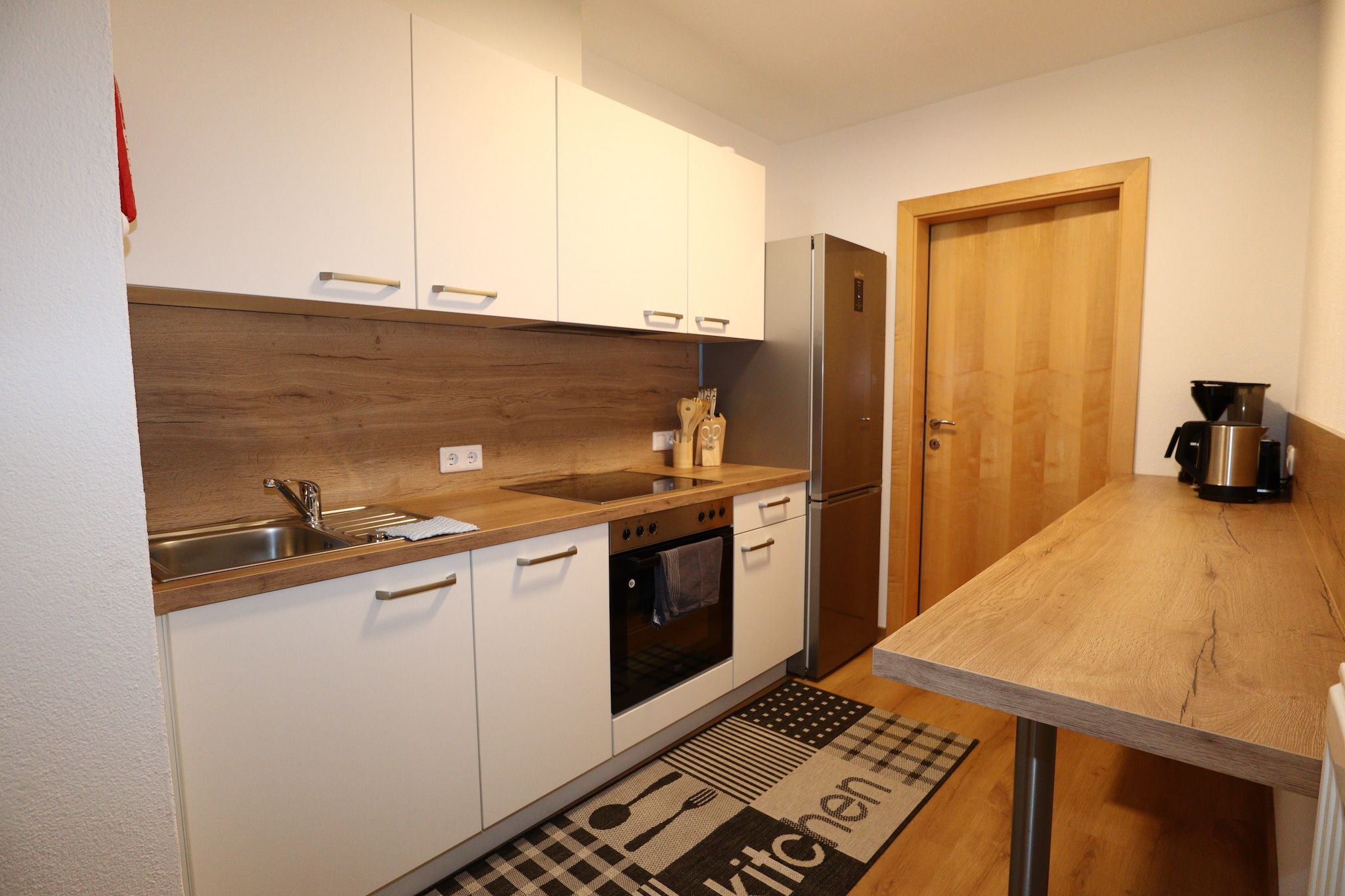 A compact kitchen with white cabinets, a wooden countertop, a built-in oven, a refrigerator, and a coffee maker.