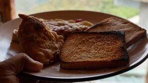 Eine Hand hält einen Teller mit Toast, Rührei und einem Stück Fleisch.