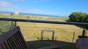 Een balkon met uitzicht op een gazon, een bankje en een hek.