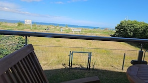 A balcony with a view of a grassy area, a bench, and a fence.