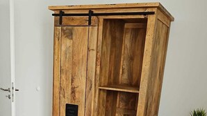 Een houten garderobe met een zwart plaquette, een bed met een geborduurd plaid en een kleine potplant op een houten tafeltje.