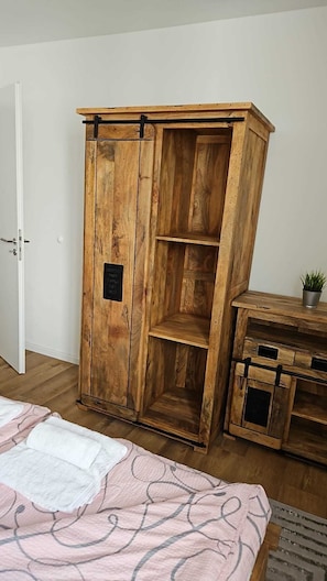 A wooden wardrobe with a black plaque, a bed with a patterned blanket, and a small potted plant on a wooden table.