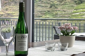 Een fles wijn, een glas en een potplant op een balkon met uitzicht op terrasservelden.