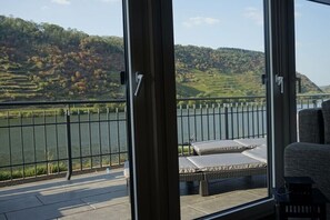 Een balkon met uitzicht op een rivier en heuvels, een stoel en een tafeltje.