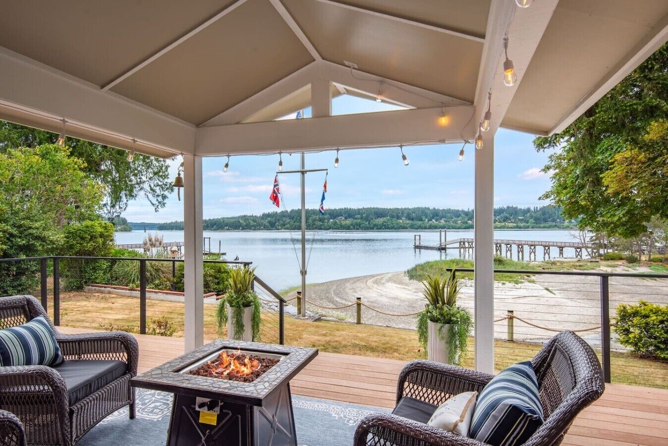 Eine überdachte Terrasse im Freien mit Korbmöbeln, einer Feuerstelle und Blick auf einen See und eine Anlegestelle.