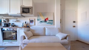 A kitchenette with a microwave, oven, and coffee maker. There is a beige sofa with pillows and a wooden table in the foreground. - Casa Vacanze Ca Zigoela (La Spezia)