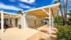 A covered outdoor area with a car parked inside, palm trees, and a tiled floor. - Le Vele della Contea (Marina Di Modica)