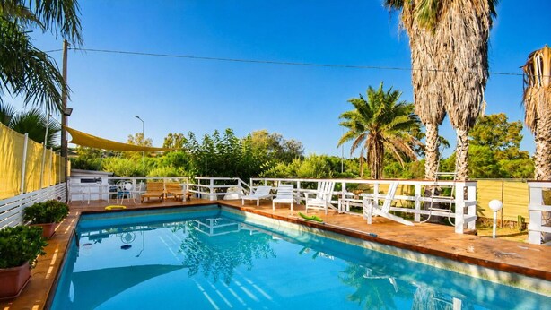 A swimming pool with a wooden deck, white lounge chairs, and a white fence. - Le Vele della Contea (Marina Di Modica)