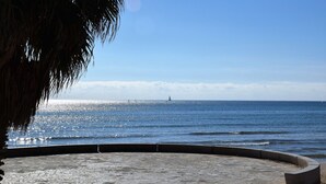 Un área costera pavimentada con vista despejada al mar y un velero a lo lejos.