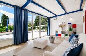 Una sala de estar moderna con un sofá blanco, cojines azules, una mesita de centro y un ventanal con cortinas azules.
