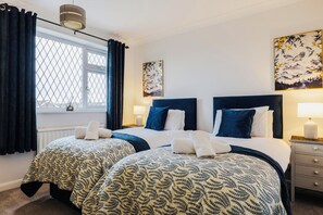 Habitación de hotel con dos camas, una ventana con cortinas, decoración en la pared y una mesita de noche con lámpara.