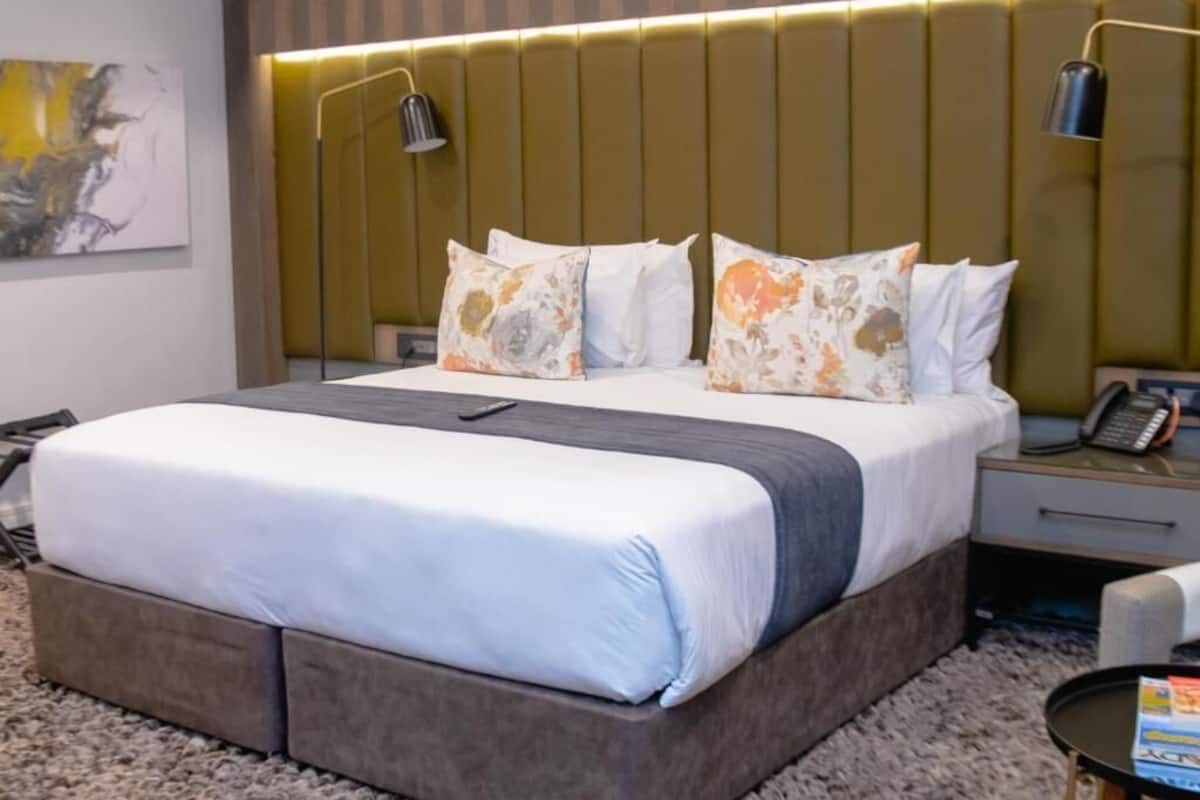 Una habitación de hotel moderna con una cama grande, una mesita de noche con lámpara y un teléfono instalado en la pared.