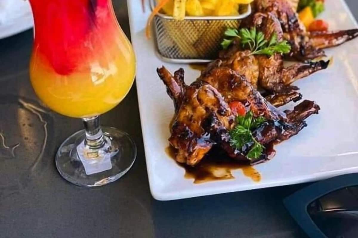 Comida con carne a la parrilla, papas fritas y una bebida roja sobre una mesa.