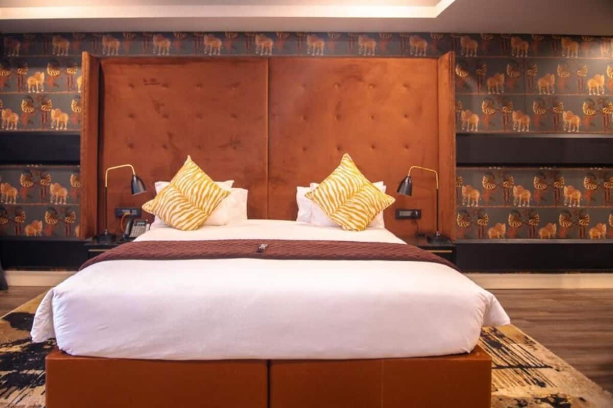 Una cama con cabecera de madera, dos lámparas y almohadas estampadas.